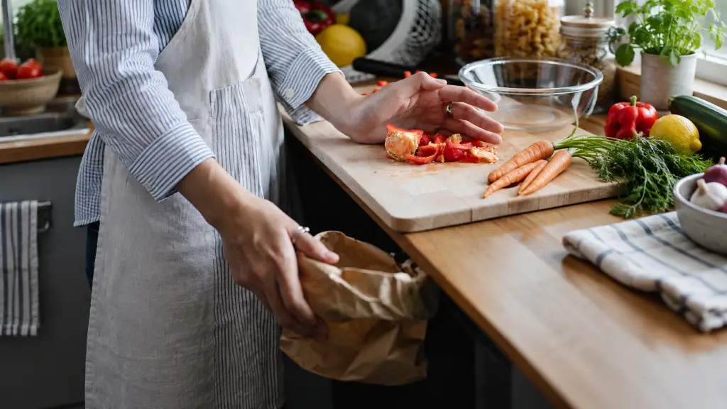 Kitchen worker holding a collection sack beside vegetable trimmings on a cutting board