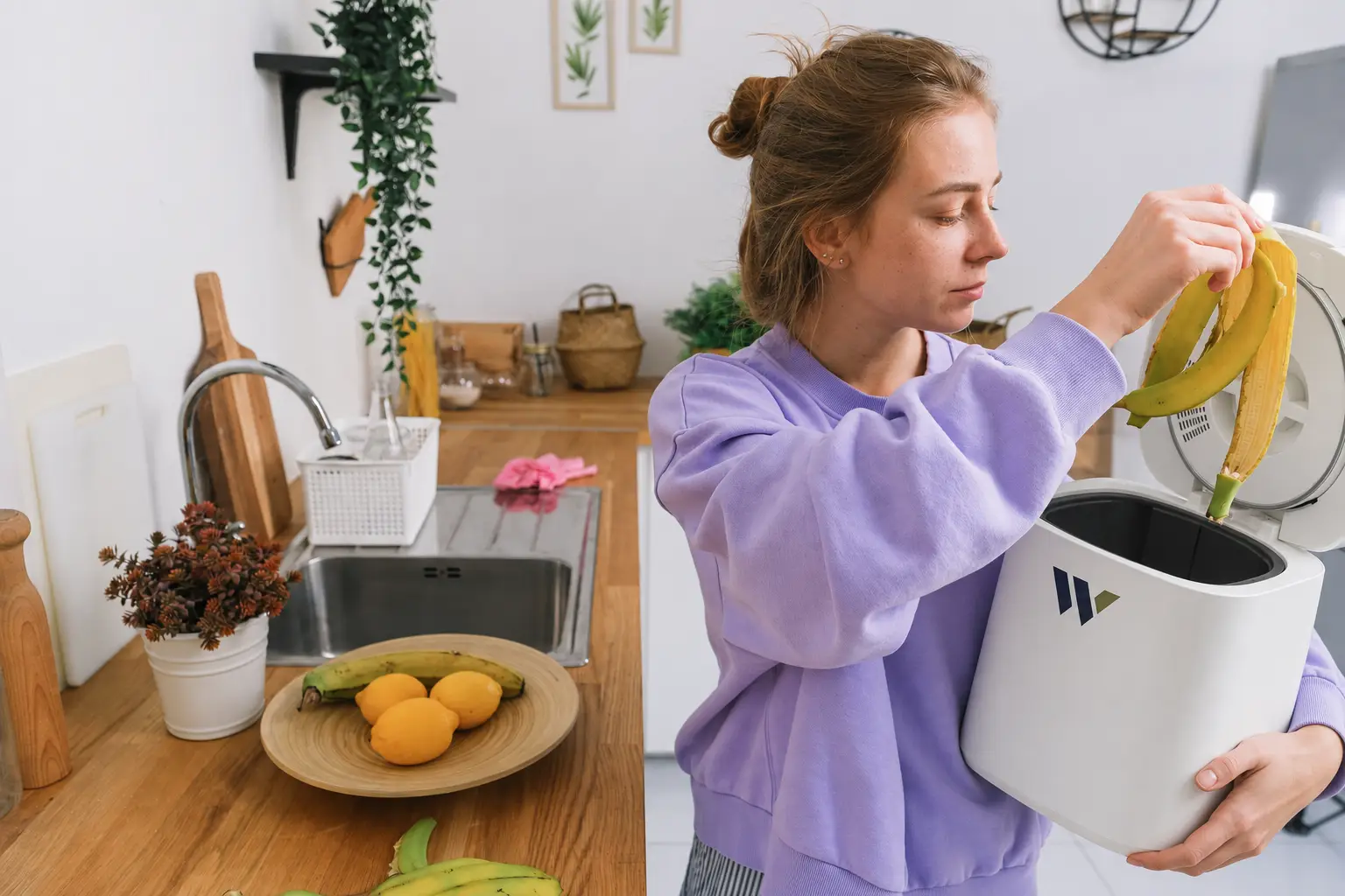 Woman placing banana peels into a Wawli household food-waste appliance in a kitchen